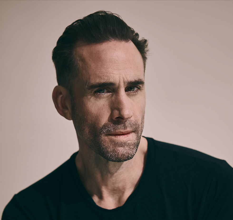 a man with short dark hair wearing a black shirt against a soft background