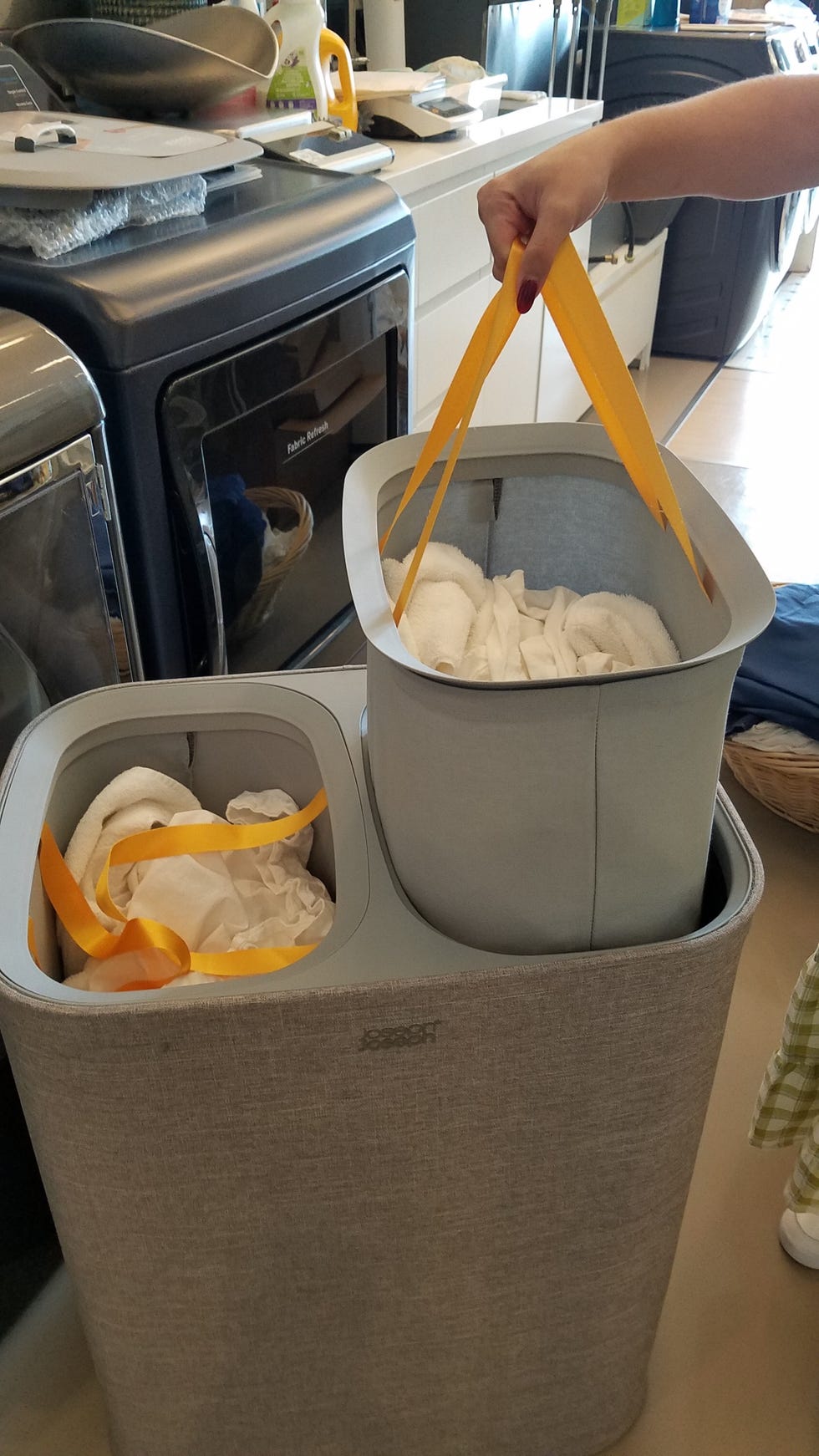 a hand lifting one bag of laundry from a gray joseph joseph laundry hamper in the good housekeeping institute cleaning lab