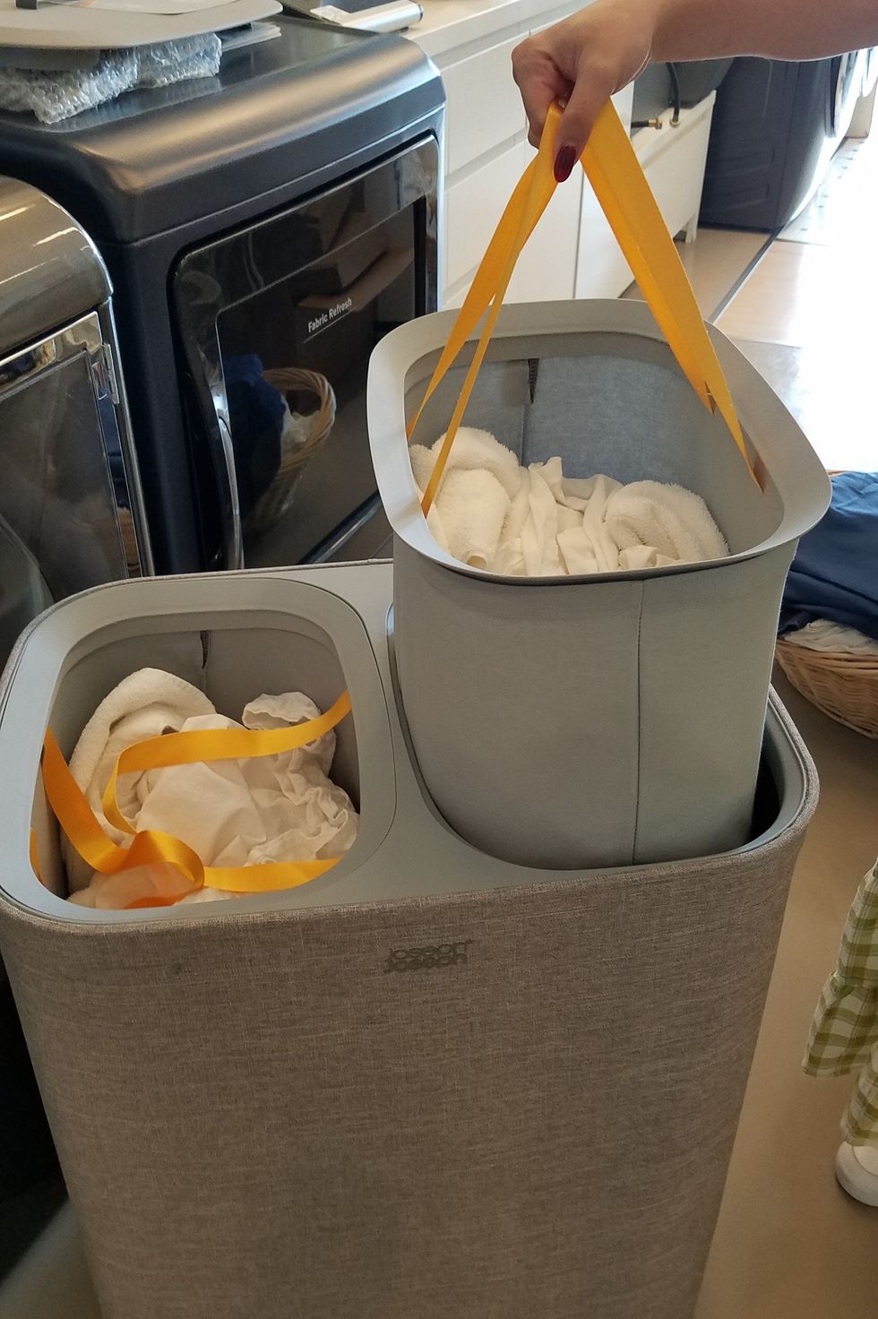 a hand lifting one bag of laundry from a gray joseph joseph laundry hamper in the good housekeeping institute cleaning lab
