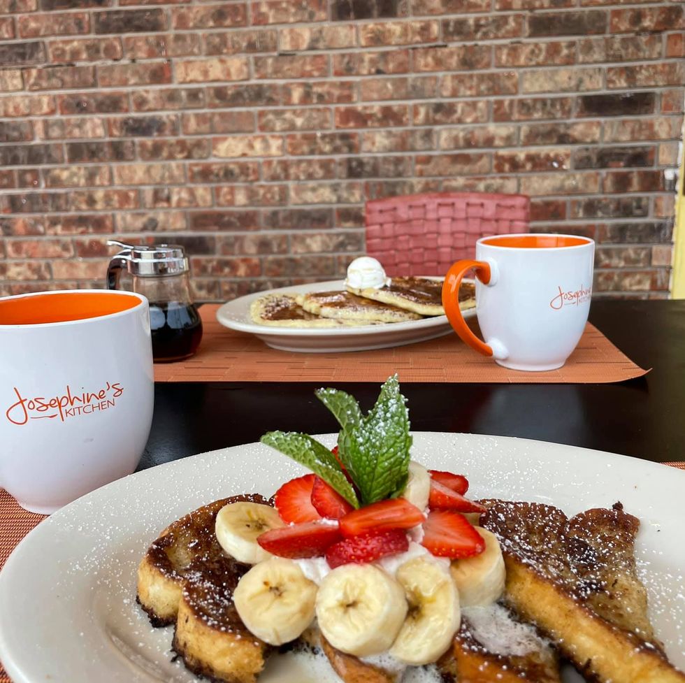 a plate of french toast with bananas and strawberries and mugs of coffee