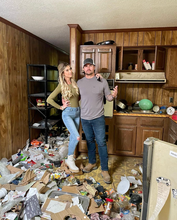 a man and woman standing in a kitchen with a pile of cardboard