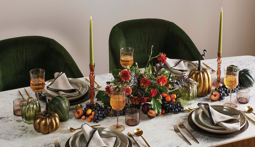 Thanksgiving Tablescape Ideas a beautifully arranged dining table featuring a variety of dishes and decorative elements the table is set with elegant plates, napkins, and cutlery, complemented by colorful floral arrangements decorative pumpkins in various colors and shapes are placed among fresh fruits like grapes and peaches tall candles in holders provide a warm ambiance against a backdrop of green velvet chairs