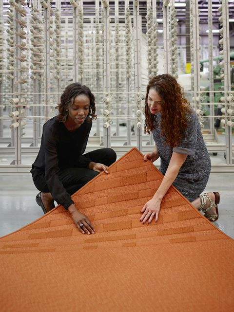 two women inspect an orange colored rug at the merida studio