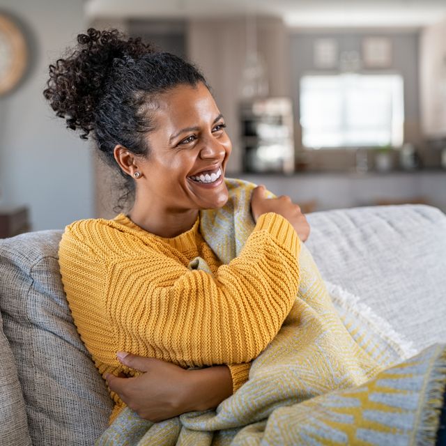 joyful woman with blanket on couch laughing