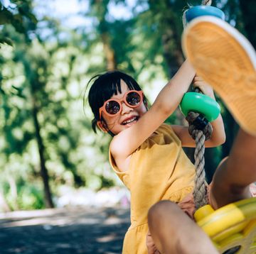 joyful little asian girl with sunglasses having fun playing on a zipline in an adventure park outdoors on a sunny day adventurous and active lifestyle of children outdoor fun
