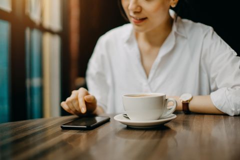 joyful young woman having a relaxing time in cafe enjoying coffee and text messaging on smartphone