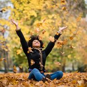 fall instagram captions  woman sitting in a pile of leaves with arms in the arm and leaves falling around her