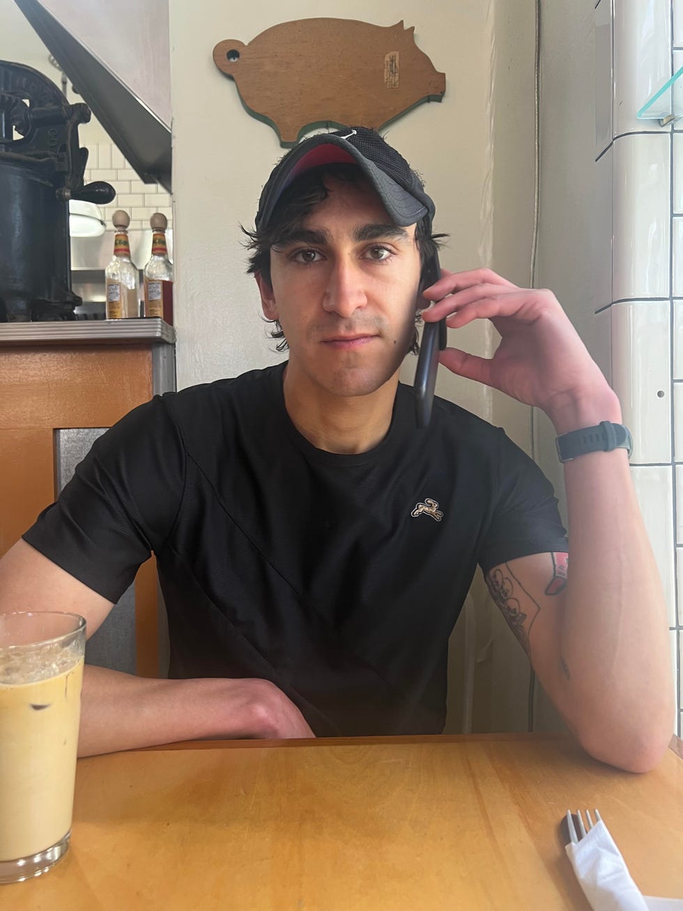 a person seated at a table engaged in a phone conversation with a drink beside them