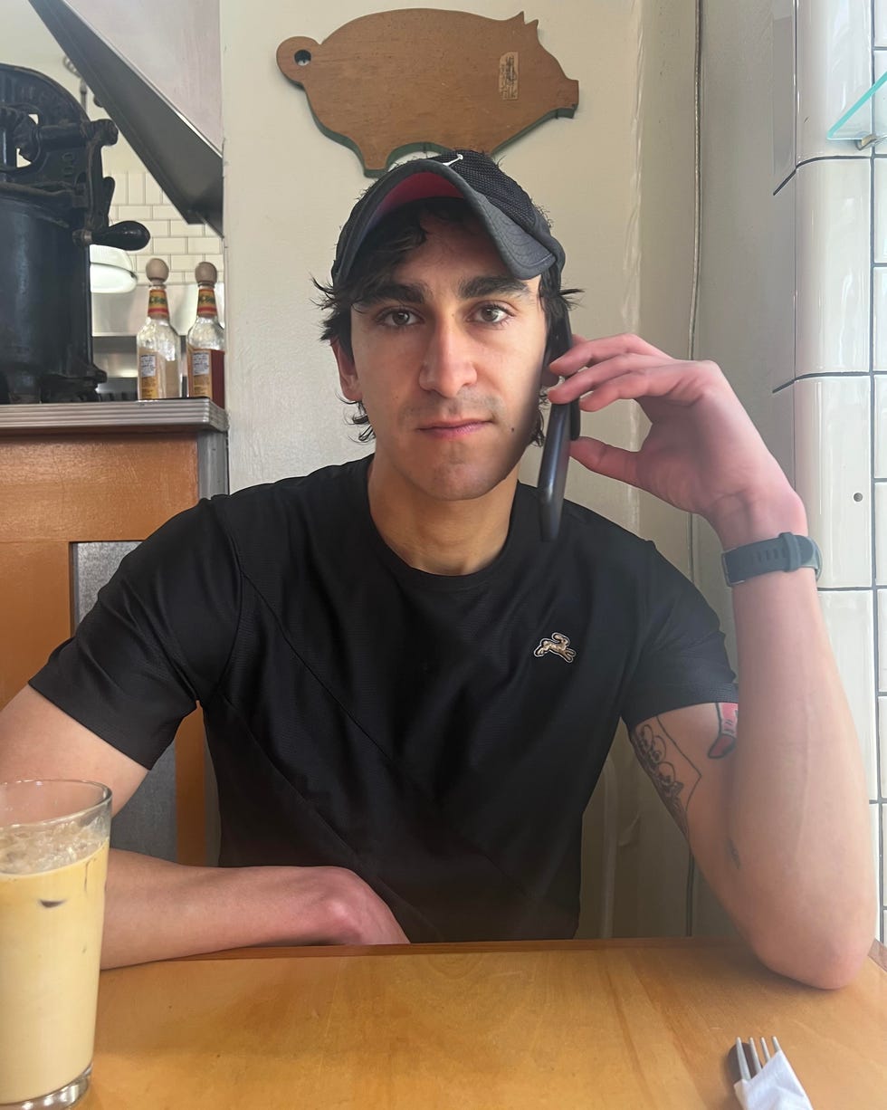 a person seated at a table engaged in a phone conversation with a drink beside them