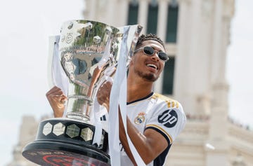 jude bellingham wears sunglasses and smiles broadly as he holds the la liga trophy with both hands