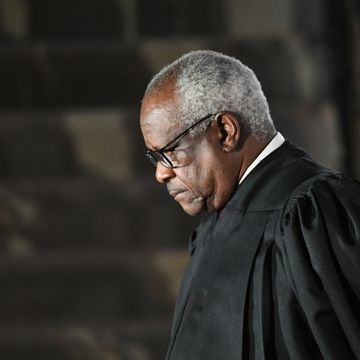 supreme court justice clarence thomas, seen in profile, is standing while wearing his black justice robes and black glasses, he is looking down with a neutral expression on his face