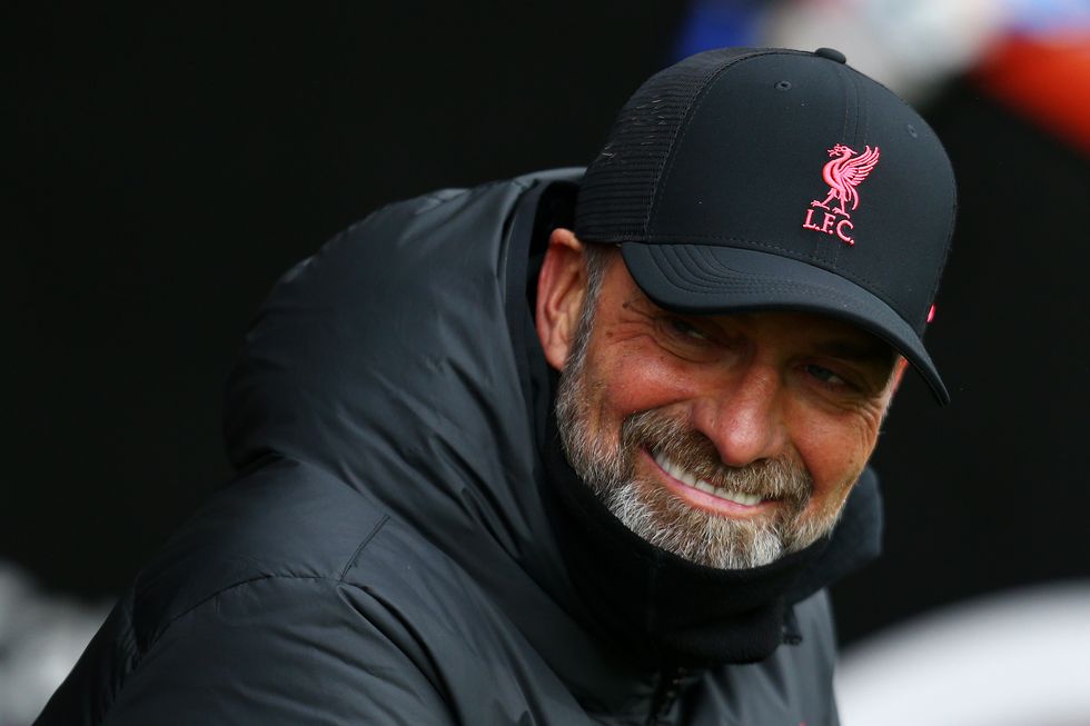 jurgen klopp wearing a black coat and hat smiles and looks off camera