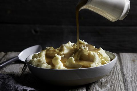 jug of gravy being poured onto bowl of steaming mashed potatoes, studio shot
