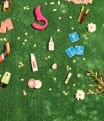 juguetes sexuales sostenibles aceites, consoladores, preservativos, velas, succionador de clítoris en un fondo de césped verde con flores