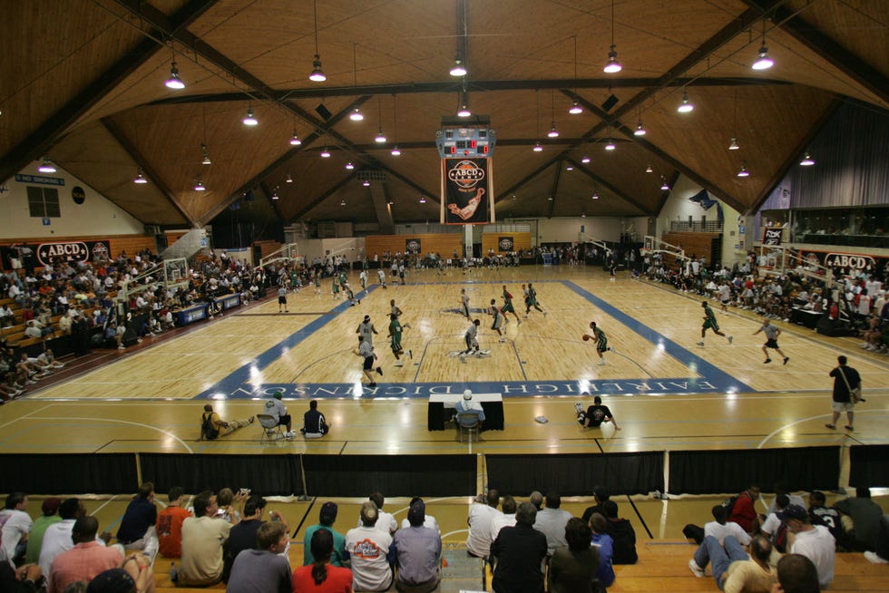 two teams play basketball in an indoor court with many people in the stands