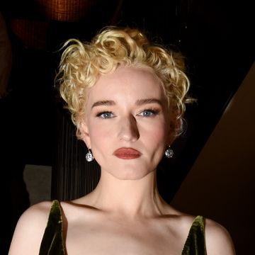 julia garner stares at the camera, she wears a velvet green dress and silver dangling earrings