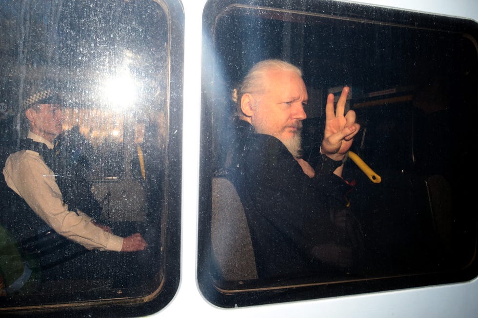 julian assange giving a peace sign through the window of a police vehicle