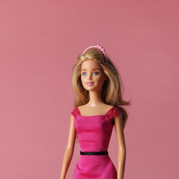 a blonde barbie doll wears a pink dress with a black belt and a pink headband