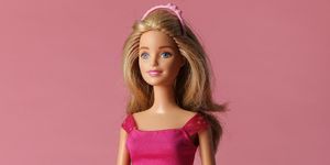a blonde barbie doll wears a pink dress with a black belt and a pink headband