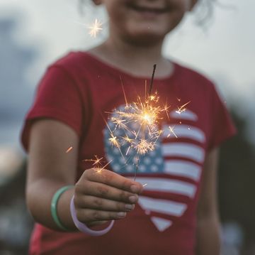 midsection of girl holding lit sparkler wearing red shirt with heart shaped american flag on front