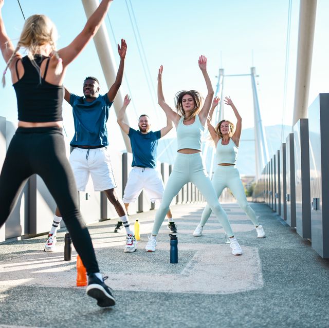 jumping jacks by female fitness instructor while working with multiethnic group outside