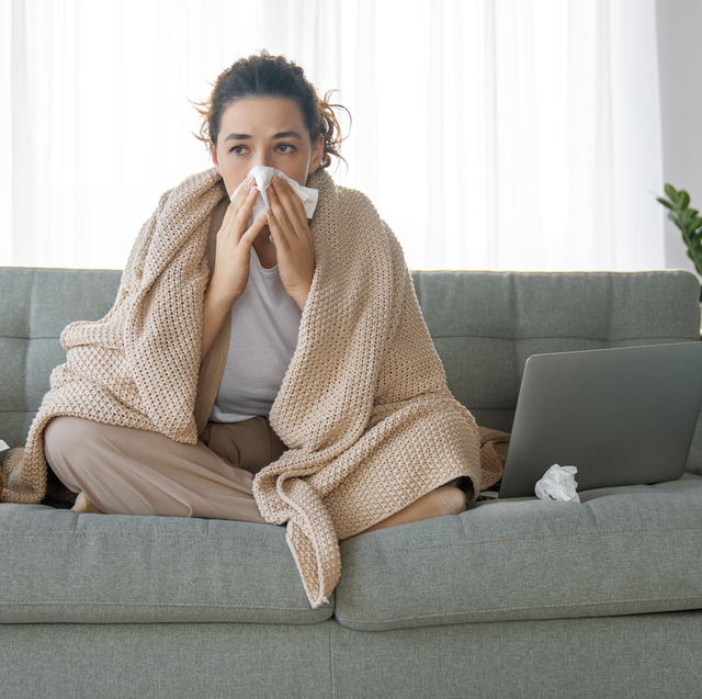 woman blowing her nose sitting on a sofa