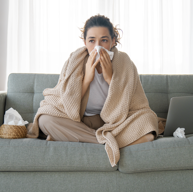 woman blowing her nose sitting on a sofa