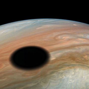 In deze opname van de NASAsonde Juno is te zien hoe Jupiters maan Io  een wereld van vulkanisme die elke 42 uur nmaal om de reuzenplaneet draait  zijn schaduw op het Joviaanse wolkendek werpt