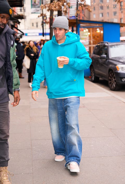 justin bieber, wearing a blue hooded sweatshirt, gray hat, and jeans, walking down a city sidewalk