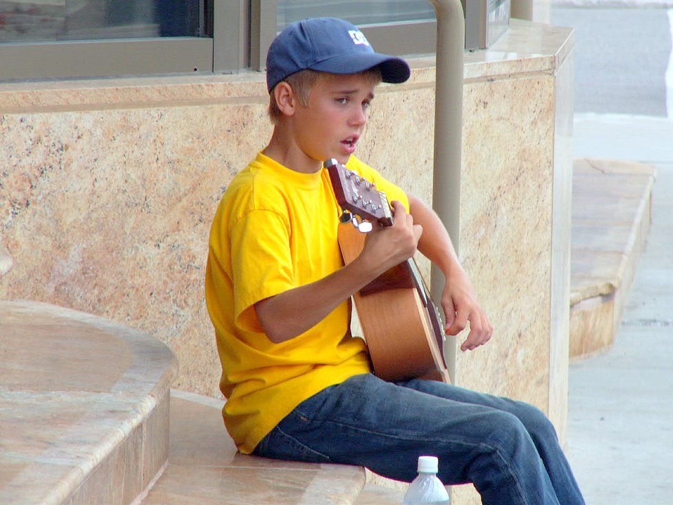 justin bieber sings as plays a guitar while sitting on the steps of a building