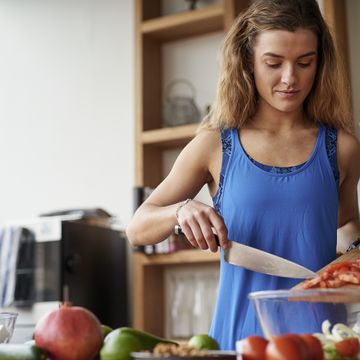 Young woman at kitchen table slicing tomatoes