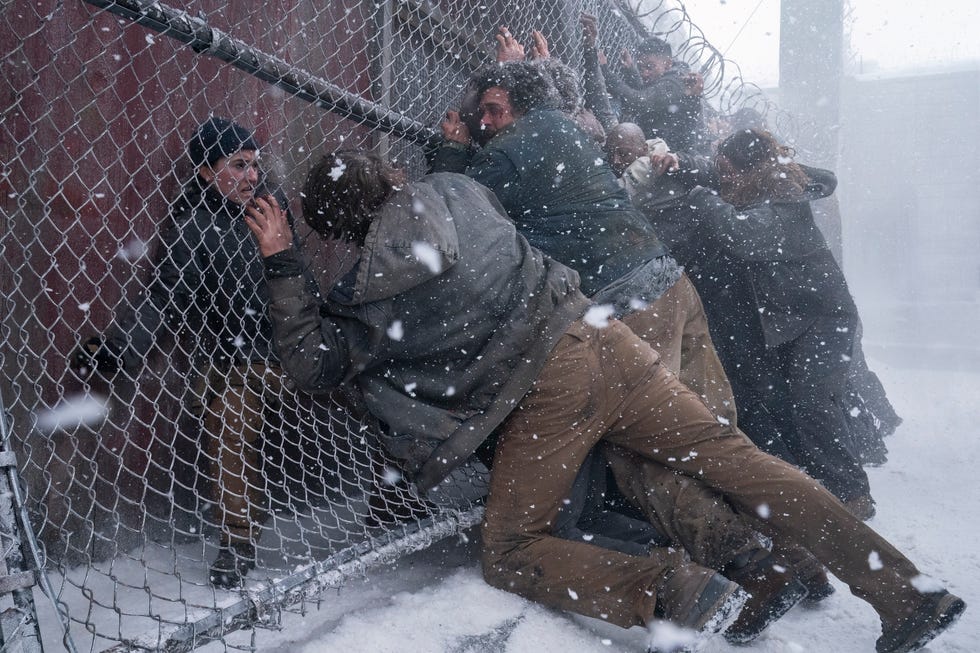 group of people struggling against a fence in snowy conditions