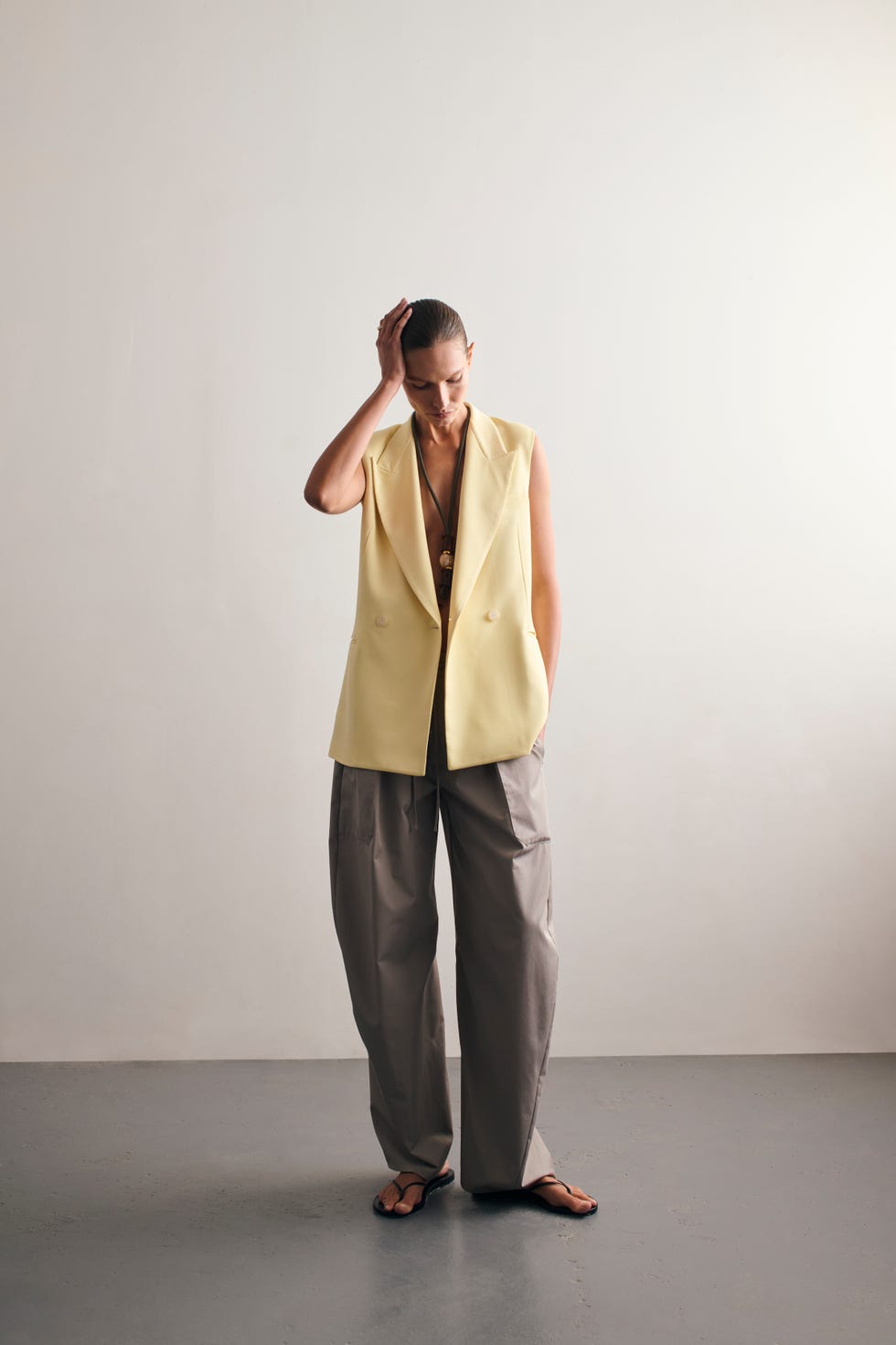 a person wearing a yellow blazer and gray trousers stands in a minimalist setting