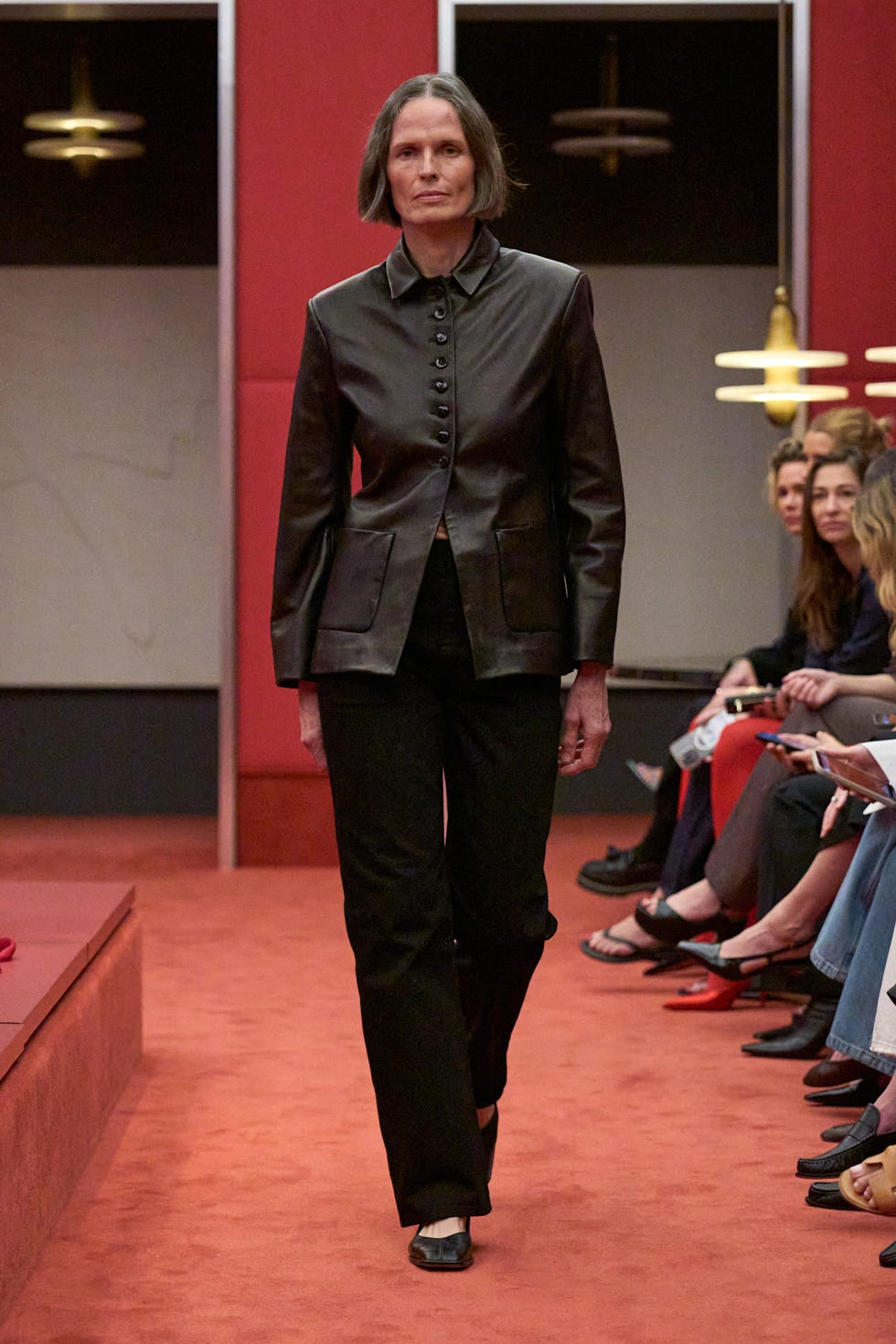 Fashion model walking on a runway featuring a dark leather jacket and black pants
