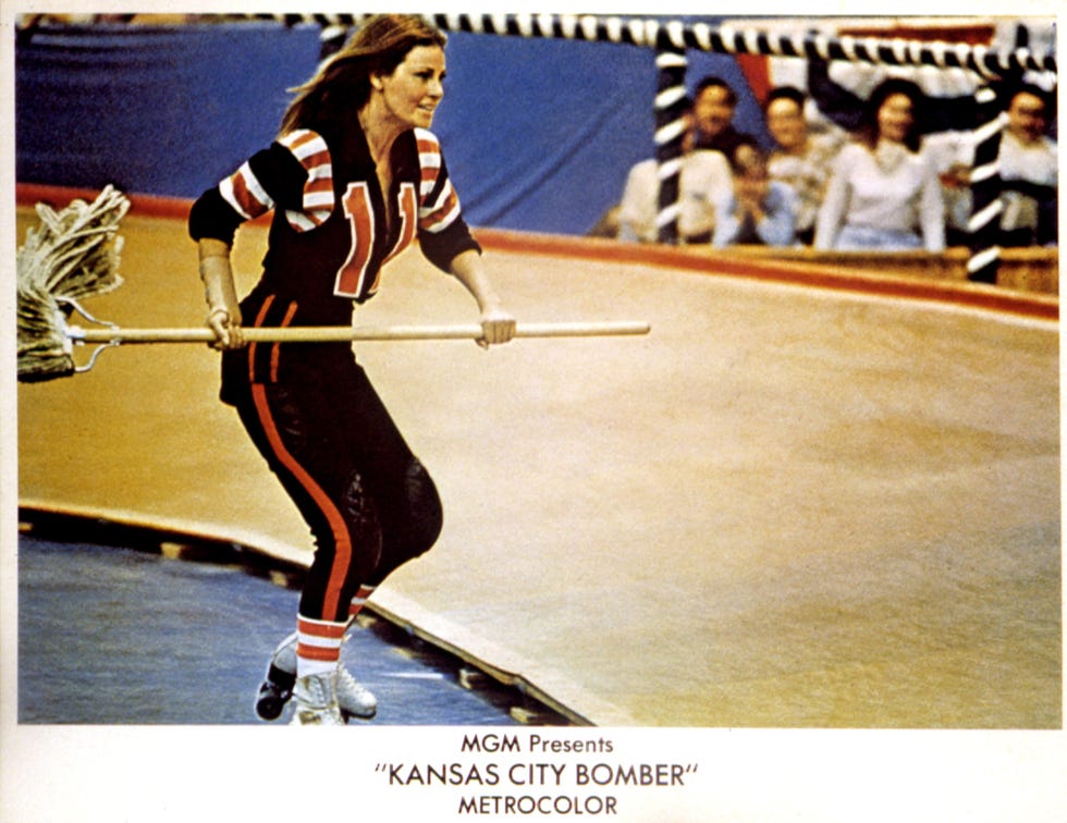 raquel welch wearing roller skates and a blue costume with the number 11 on it, holding a mop and skating on a roller rink while fans cheer in the background