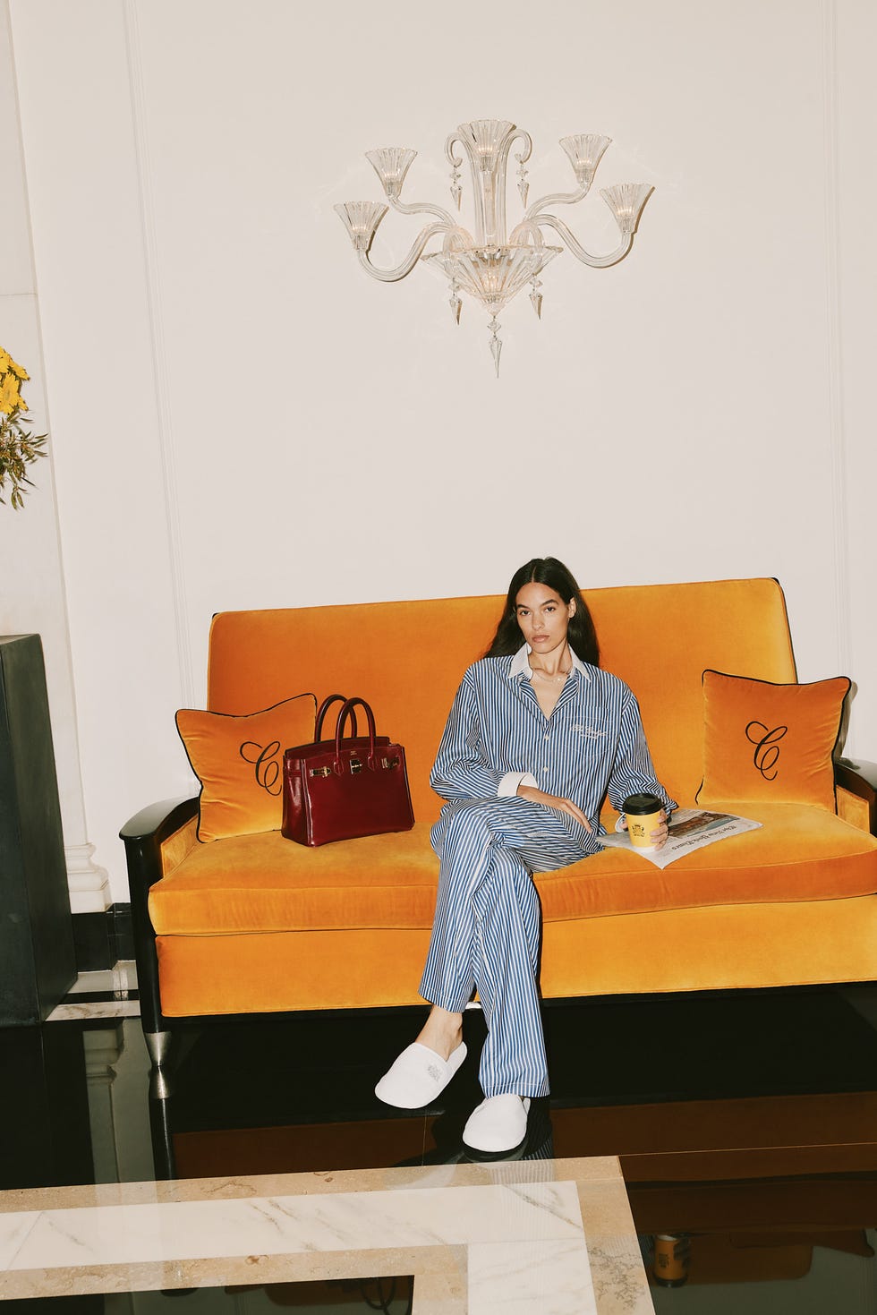 person on an orange sofa holding a cup of coffee and a magazine