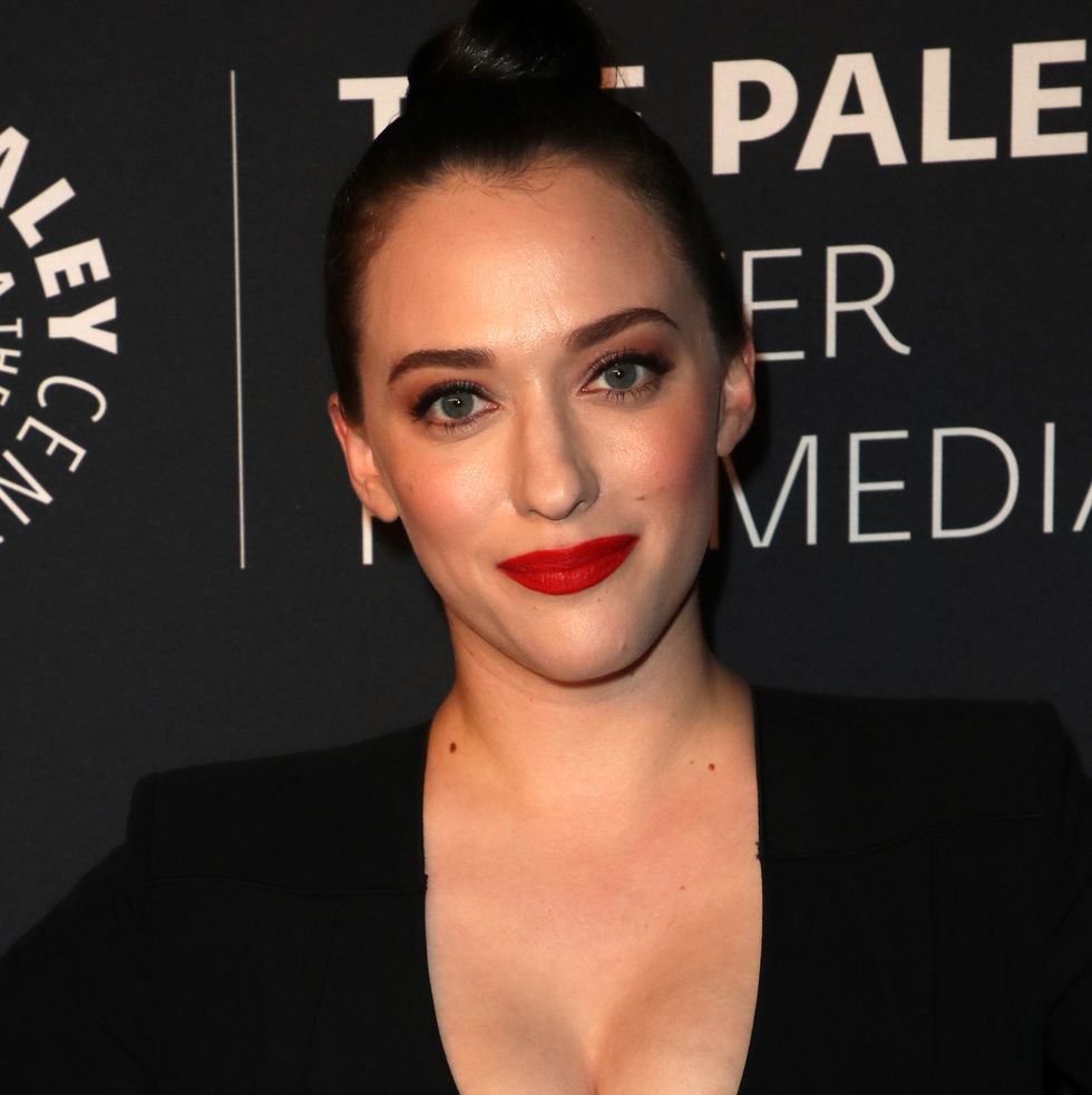 kat dennings smiling with red lipstick, wearing hair in bun and black top