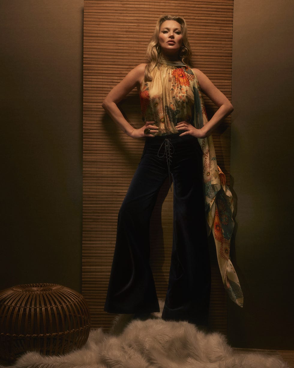 kate moss stands wearing black velvet trousers and a floral silk shirt