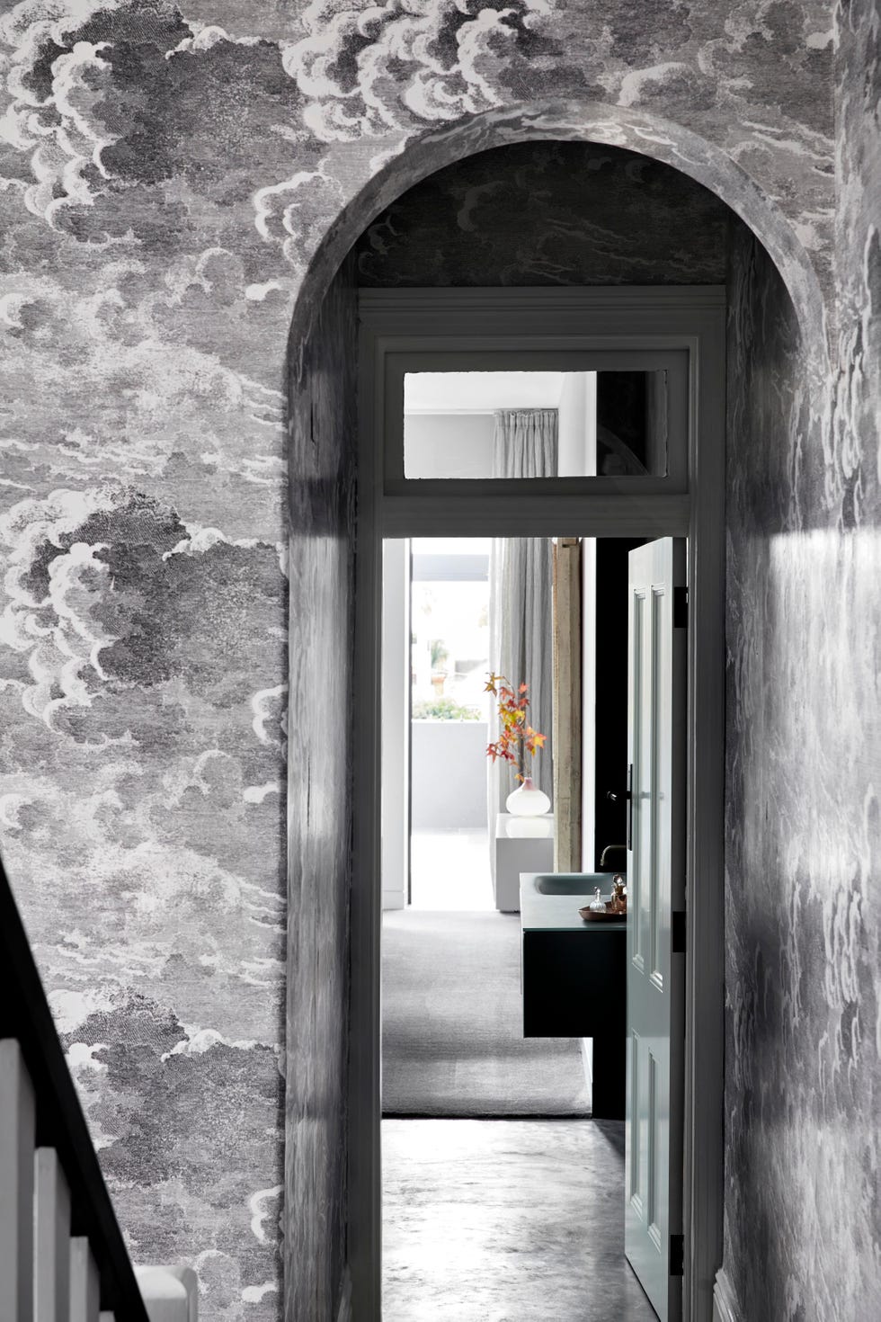 arched doorway looking into bathroom with walls covered in black and white cloud wallpaper