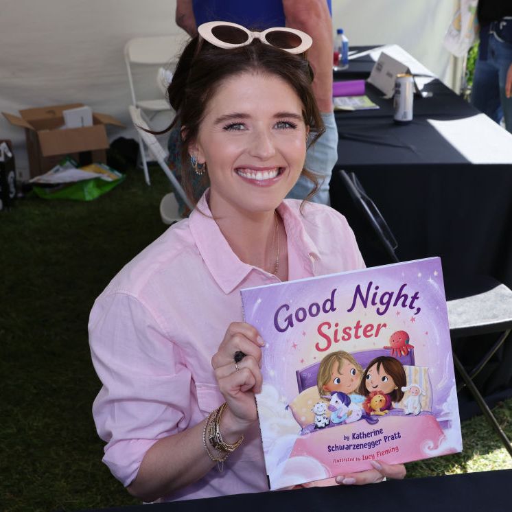 katherine schwarzenegger pratt holding up her book for the camera and smiling while sitting at a table