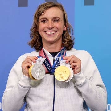 Katie Ledecky at the 2020 Tokyo Olympics in July 2021 katie ledecky smiles and displays four olympic medals hanging from her neck, she wears a long sleeve cream colored jacket
