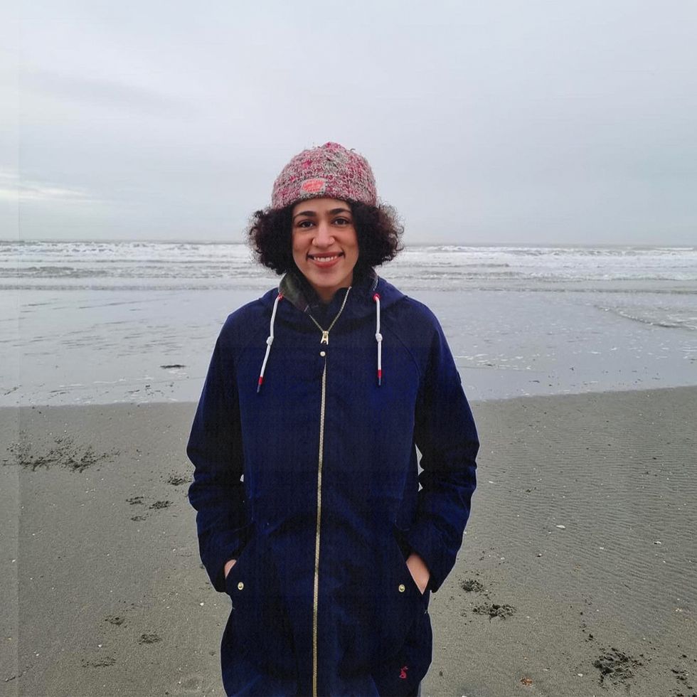 the writer, katya, standing on a beach and smiling wearing a wooly hat and jacket as it is a cold december day