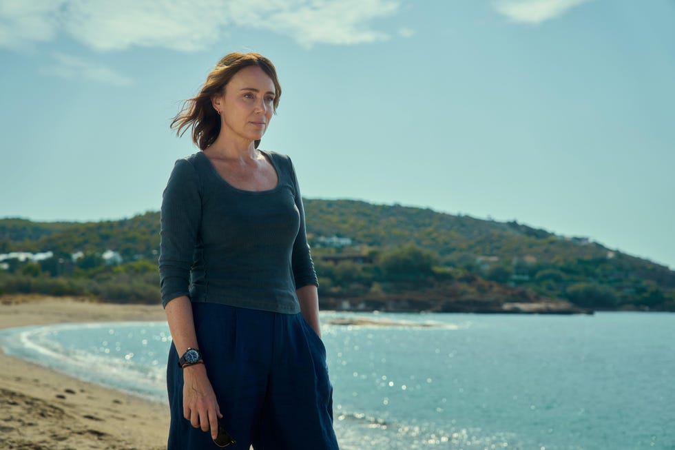 a woman standing by the beach near water and hills