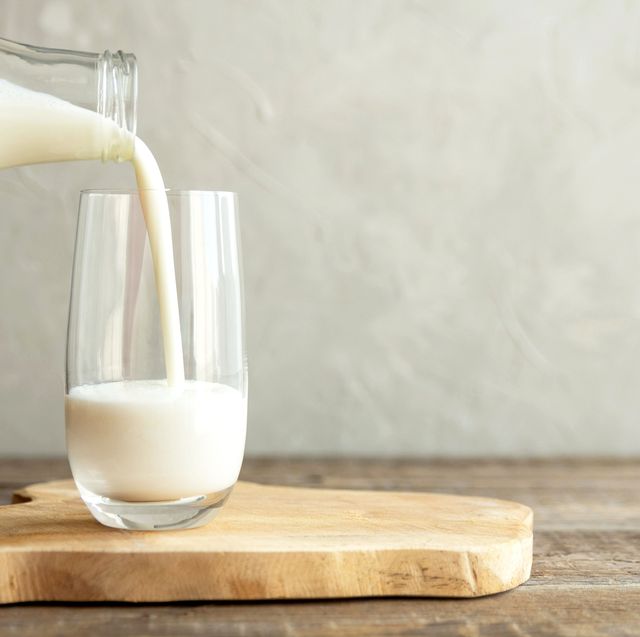 kefir, milk or turkish ayran drink are poured into a glass cup from a bottle. a glass stands on a wooden stand on a rustic wooden table. place for text