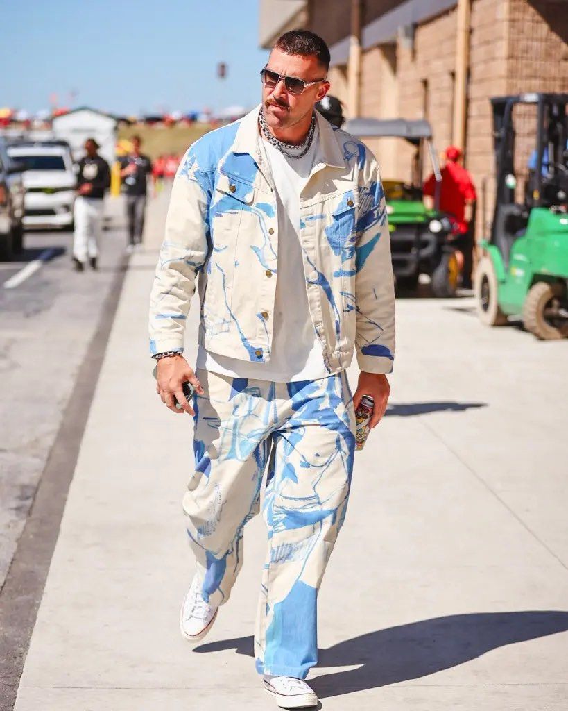 a man wearing a blue and white jacket and sunglasses walking on a sidewalk
