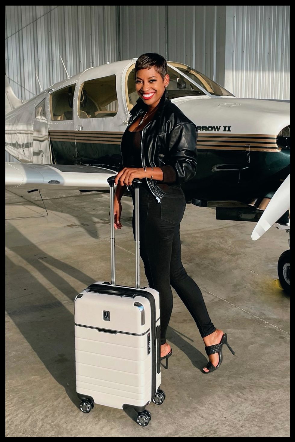 kellee edwards carries a roll on suitcase in front of a small plane in a roundup of the best carry on suitcases for travel