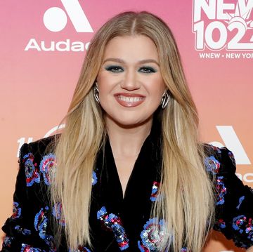 kelly clarkson poses with her hand on her waist, she wears a black dress with a blue and red floral pattern