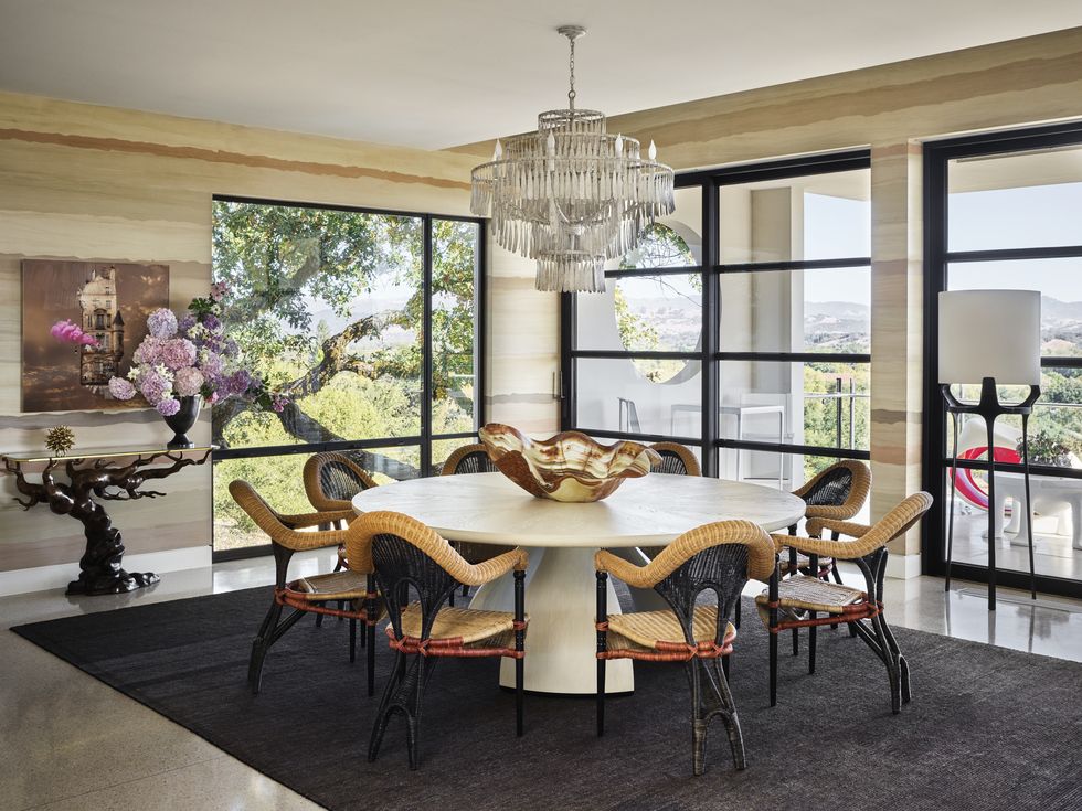 a hand painted wall mural depicts the tonal beauty of rammed earth and envelops a round dining table with chairs and a fancy chandelier hanging overhead