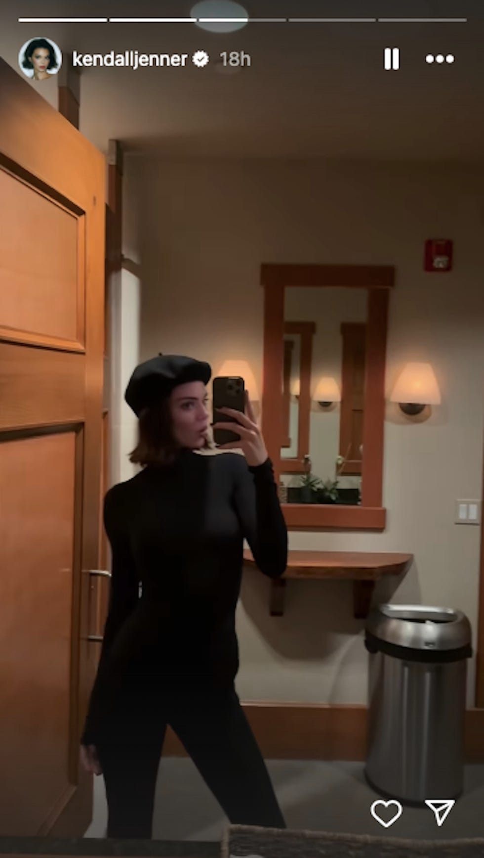 a figure taking a selfie in a room with wooden accents and a mirror