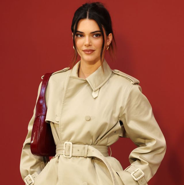 kendall jenner poses in a tan trench coat with a red purse on her shoulder